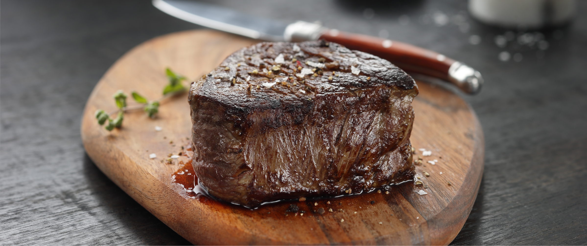 A dry-aged prime steak on a wooden serving board with thyme and salt at Chandlers Steakhouse