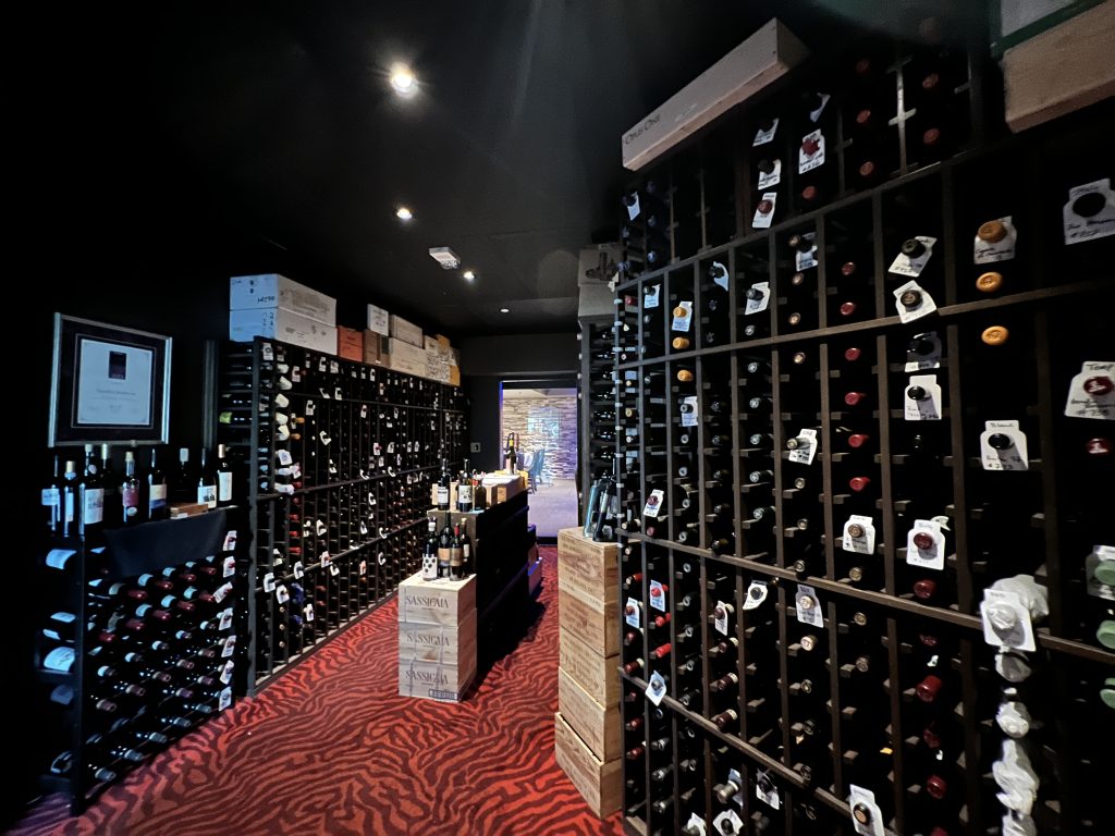 Floor-to-ceiling wine racks in Chandlers' cellar with Sassicaia wooden cases on a red carpet